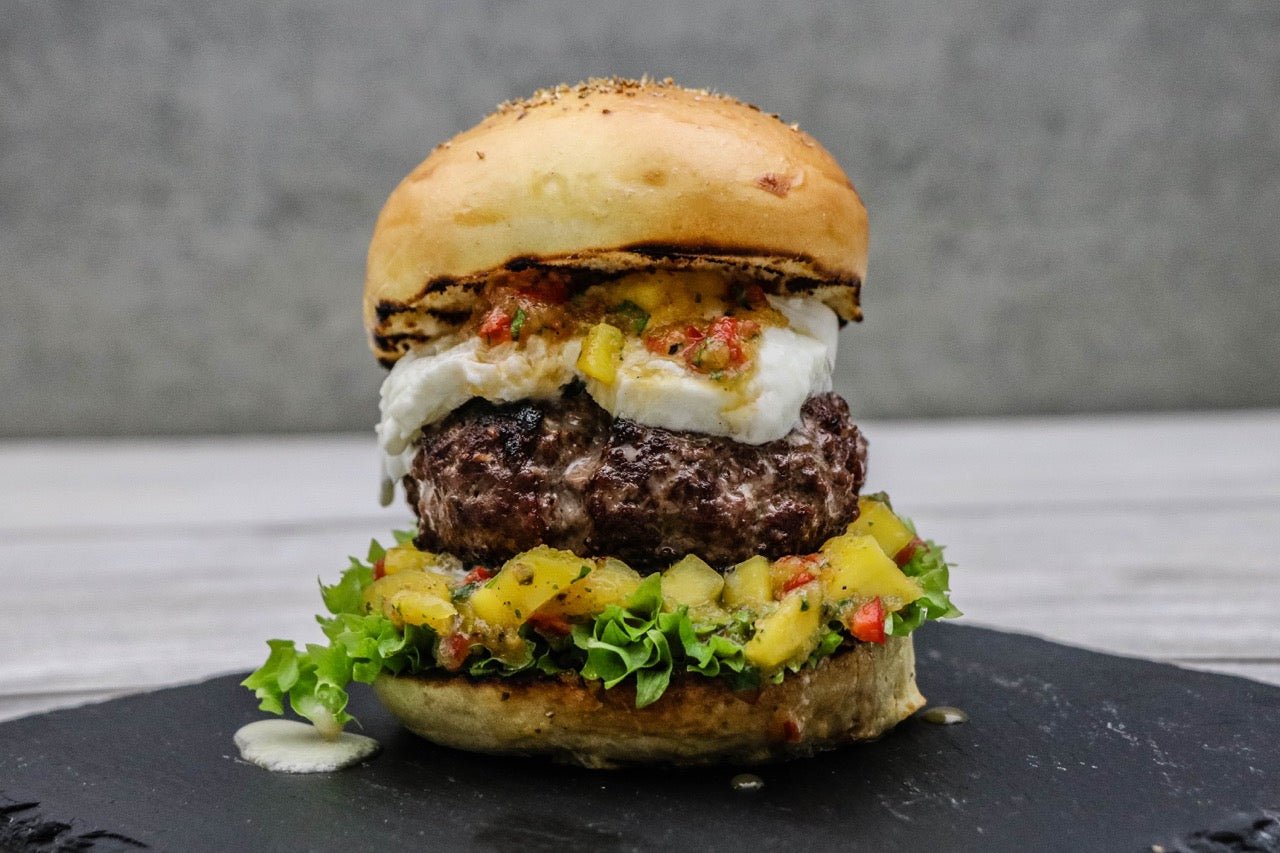 Doppelter Büffel Burger mit Mango Chili-Salsa Der doppelte Büffel Burger mit Mango Chili-Salsa ist ein absolutes Highlight! 180 Gramm saftiges Büffelfleisch mit Premium Büffelmozzarella im frisch gebackenen Brioche Bun. Eine köstliche Kreation von Marcel